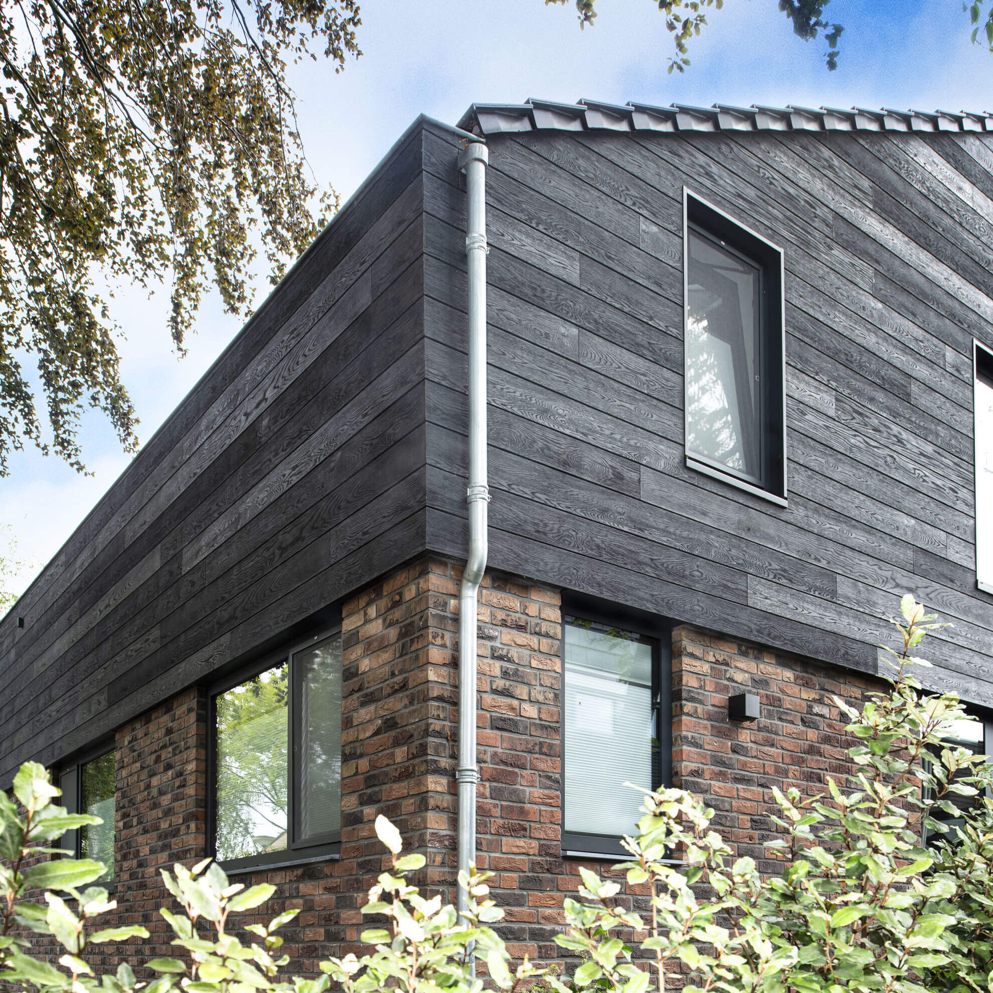 Hoek van de woning met donkere planken boven de bakstenen gevel