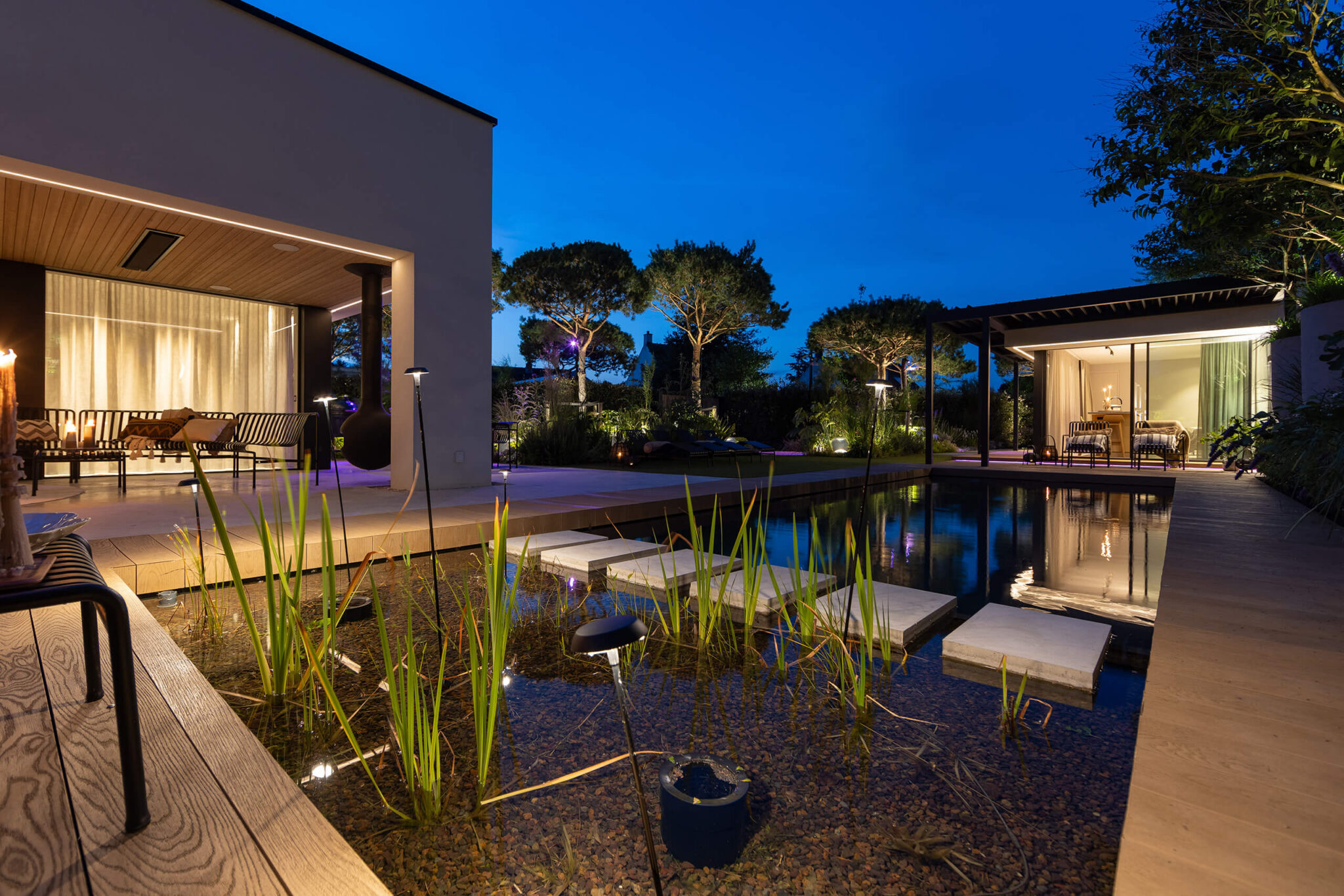 Kusttuin met verlicht zwembad en poolhouse in de avond