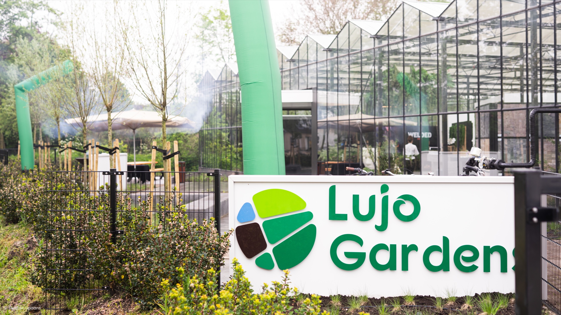 De glazen entree van het LujoGardens inspiratiecenter in Uden, met het Lujo Gardens bord op de voorgrond.